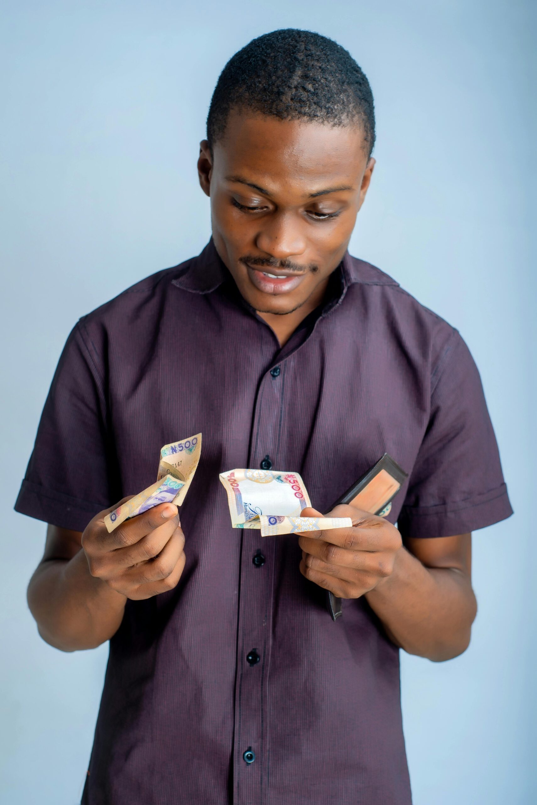 African man in a studio counting Nigerian naira banknotes with a wallet in hand.